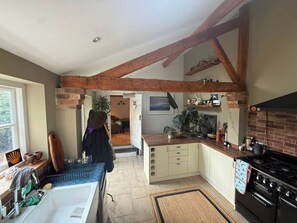 A kitchen with exposed wooden beams, a stove, cabinets, and a window.