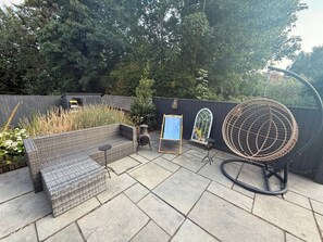 A patio with a wicker sofa, a small table, a hanging chair, and a decorative mirror.