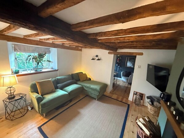 A cozy living room with a green sectional sofa, a small side table, a lamp, and a TV on a wooden stand.