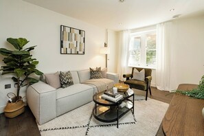 Ein modernes Wohnzimmer mit einer Couch, einem Sessel, einem Couchtisch und einer großen Pflanze.
