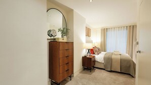 Une chambre à coucher avec un lit, une commode, une table de chevet, une lampe et une fenêtre avec des rideaux.