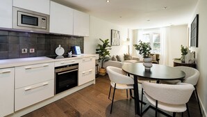 Une cuisine moderne avec des meubles blancs, un four à micro-ondes encastré et un coin repas comprenant une table ronde et des chaises.