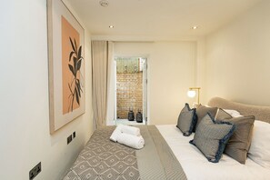 A hotel room with a bed, a bedside lamp, a towel, a picture on the wall, and a view of the outside. - 2BR Duplex Flat near Buckingham Palace (London)