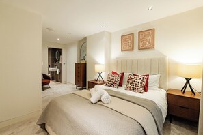 A hotel room with a bed, bedside tables, a nightstand, a mirror, and a bathroom visible through an open door. - 2BR Duplex Flat near Buckingham Palace (London)