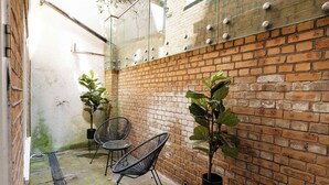 Un mur de briques avec un panneau de verre, deux chaises et des plantes en pot.