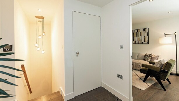 Un couloir avec une porte blanche, un luminaire suspendu et une plante.
