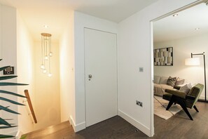 A hallway with a white door, a hanging light fixture, and a plant. - 2BR Duplex Flat near Buckingham Palace (London)