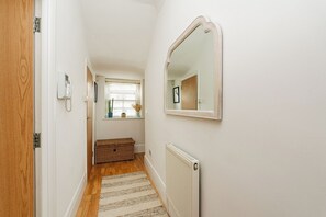 A narrow hallway with a wooden door, a radiator, a mirror, and a window with plants. - Bright 1BR Flat Opposite Peckham Rye Park (London)