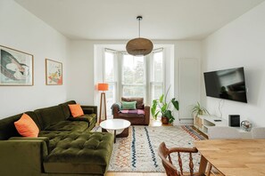 Ein Wohnzimmer mit einem grünen Sofa, einem Couchtisch, einem Fernseher und einem Essbereich mit Stühlen.
