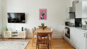 Une cuisine moderne avec des meubles blancs, une table à manger en bois et un téléviseur à écran plat fixé au mur.