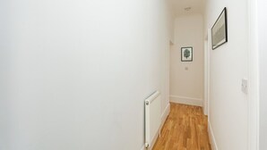 Un couloir étroit aux murs blancs, avec un radiateur et un plancher en bois.