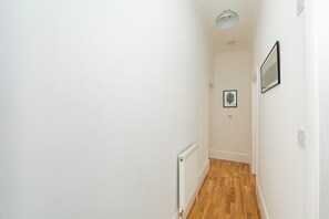 A narrow hallway with white walls, a radiator, and a wooden floor. - Bright 1BR Flat Opposite Peckham Rye Park (London)
