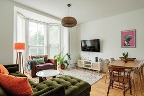 A living room with a sofa, a coffee table, a TV, and a dining area with chairs and a table. - Bright 1BR Flat Opposite Peckham Rye Park (London)