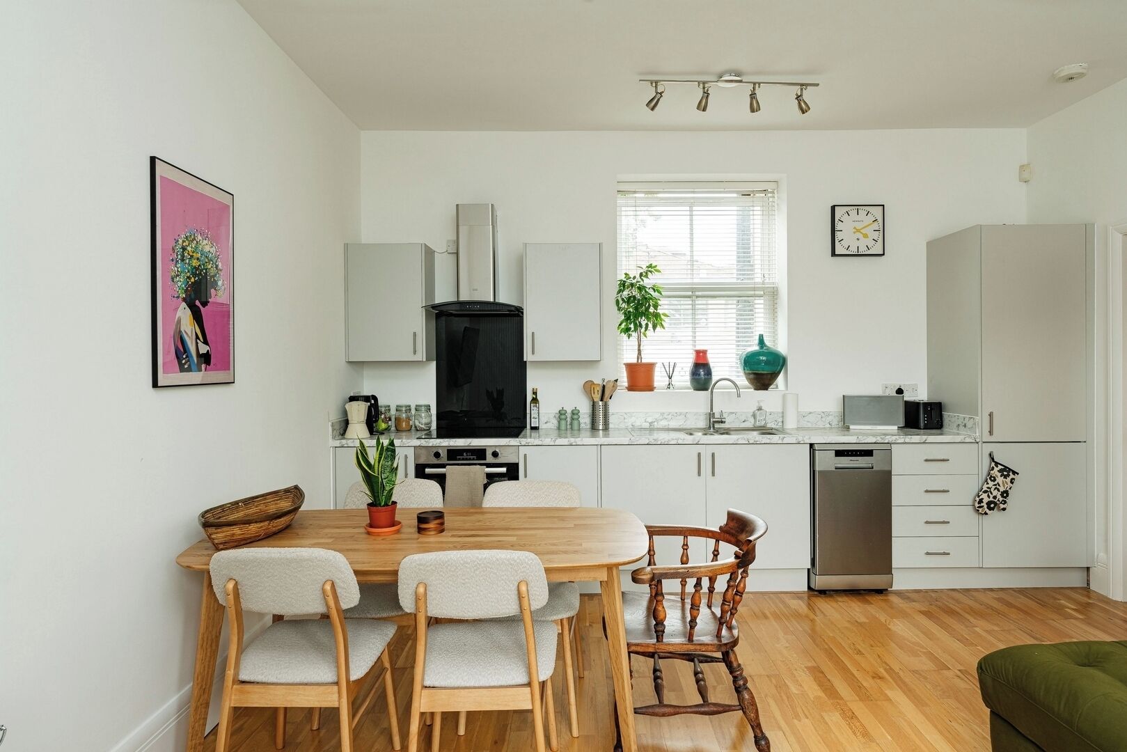 Une cuisine moderne avec des meubles blancs, une cuisinière noire et un coin repas comprenant une table et des chaises en bois.