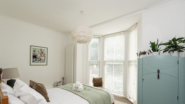 Une chambre à coucher avec un lit, une table de chevet, une lampe et une grande fenêtre avec des stores.