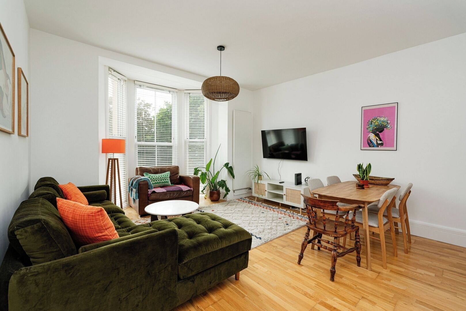 Een woonkamer met een groene bank, een eettafel en een aan de muur bevestigde televisie.