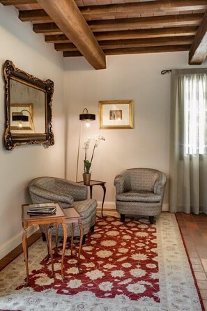 A room with two armchairs, a small table, a floor lamp, a mirror, and a patterned rug. - Villa Lampina - private villa on luxury estate (Varignana-Palesio)