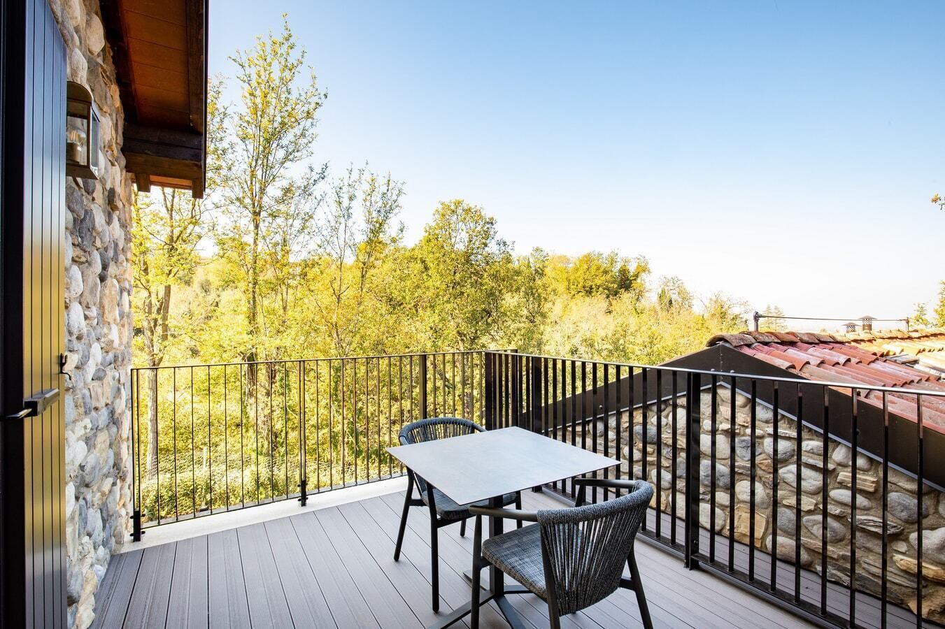 A balcony with a table and chairs, stone walls, and a view of trees.