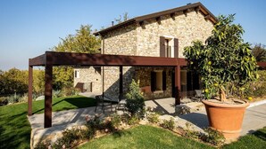 A stone house with a covered patio, a large potted plant, and a lawn. - Villa Lampina - private villa on luxury estate (Varignana-Palesio)