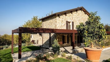 A stone house with a covered patio, a large potted plant, and a lawn.