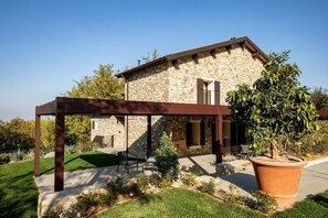 A stone house with a covered patio, a large potted plant, and a lawn. - Villa Lampina - private villa on luxury estate (Varignana-Palesio)