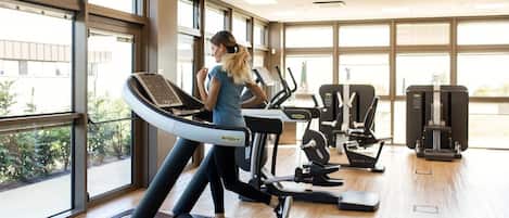 A gym with a treadmill, weight machines, and large windows.