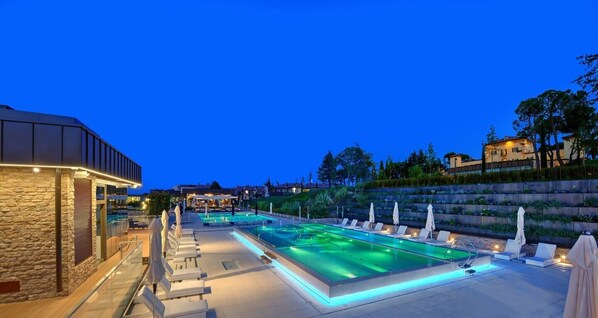 A pool area with lounge chairs and umbrellas, surrounded by stone walls and vegetation.