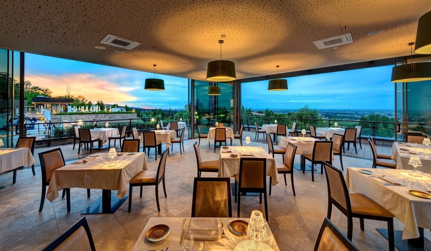 An indoor dining area with tables and chairs, large windows, and pendant lighting.