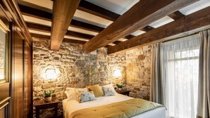 A bedroom with a stone wall, a wooden ceiling, a bed with a gold bedspread, and two wall-mounted lamps. - Villa Lampina - private villa on luxury estate (Varignana-Palesio)