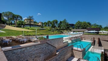 A pool area with multiple swimming pools, outdoor seating, and a stone wall.