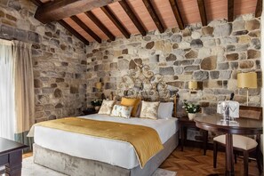 A bedroom with a stone wall, a bed with a gold headboard, a wooden table, and a lamp. - Villa Lampina - private villa on luxury estate (Varignana-Palesio)