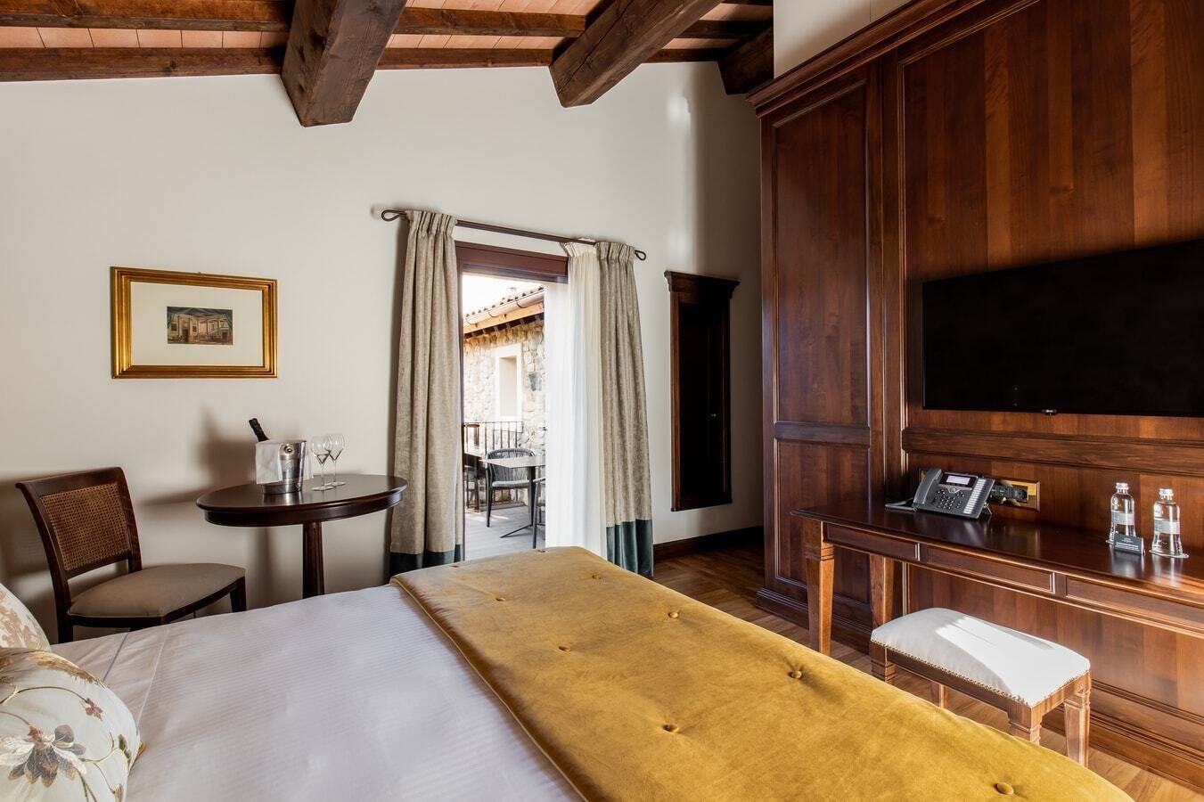 A hotel room with a bed, a desk with a telephone, a chair, and a table with a wine glass.