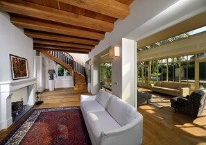 Ein großzügiger Wohnbereich mit einem weißen Sofa, einem gemusterten Teppich und einer Treppe, die in eine obere Ebene führt.