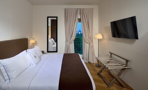 Ein Hotelzimmer mit einem Bett, einem Fernseher, einem Spiegel, einem Fenster mit Vorhängen und einer Bank.