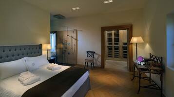 A hotel room with a bed, a chair, a table with items, a wardrobe, and a shower area.