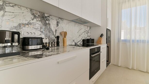 A modern kitchen with a marble backsplash, built-in appliances, and a large window with sheer curtains. - Villa Basia with private pool in Ciovo Island (Okrug Gornji)