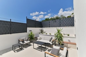 Eine Terrasse im Freien mit einer Couch, Stühlen, einem Tisch und Kübelpflanzen.