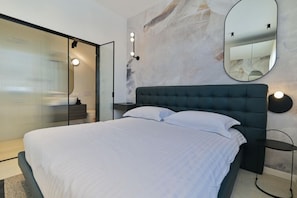 Ein modernes Schlafzimmer mit einem großen Bett, einer Glastrennwand, einem Spiegel und Wandleuchten.