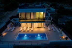 Ein modernes, zweistöckiges Haus mit Swimmingpool, Außenbereich zum Sitzen und einem Balkon.