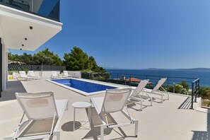 Ein Poolbereich auf dem Dach mit Liegestühlen und Blick auf das Meer.