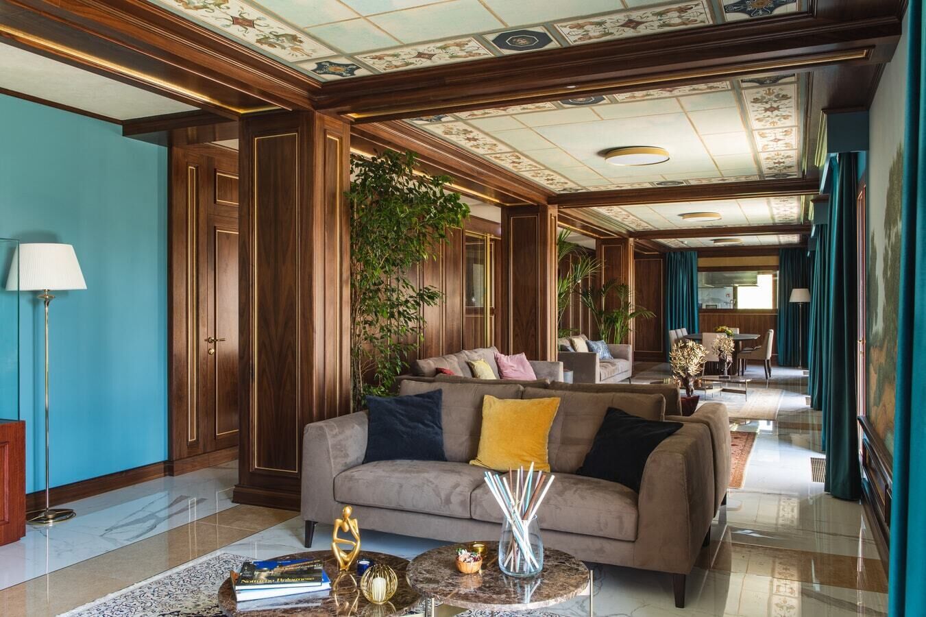 A hotel lobby with a grand wooden reception desk, a seating area with sofas, a chandelier, and a large painting on the wall.
