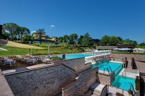 Ein Poolbereich mit mehreren Schwimmbecken, Sitzmöglichkeiten im Freien und Blick auf die umliegende Landschaft.