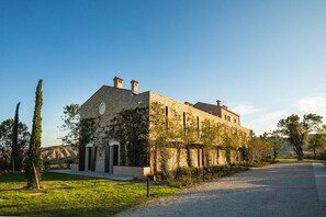 Ein zweistöckiges Steinhaus mit flachem Dach, umgeben von einem gepflegten Rasen und einem Kiesweg.