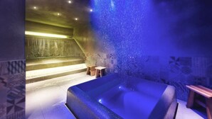 Ein Wellnessraum mit einer großen Badewanne, einem kleinen Holzschemel und einer Wand mit gemusterten Fliesen.