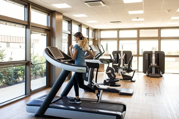 A gym with a treadmill, weight machines, and large windows.