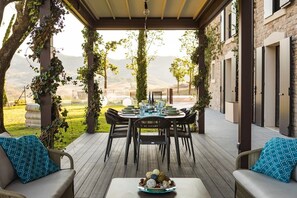 An outdoor patio with a table set for dining, surrounded by chairs and a sofa, with a view of the landscape.