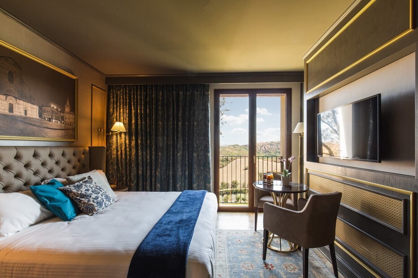 A hotel room with a large bed, a desk, a television, and a balcony with a view.