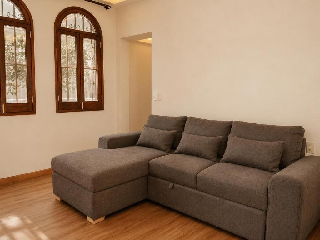 A grey sectional sofa in a room with wooden flooring and two arched windows.