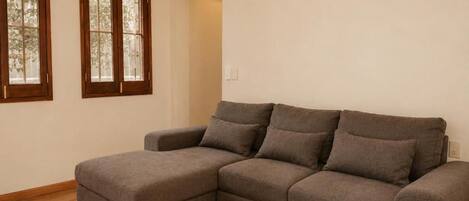Um sofá modular cinza numa sala com soalho de madeira e duas janelas em arco.
