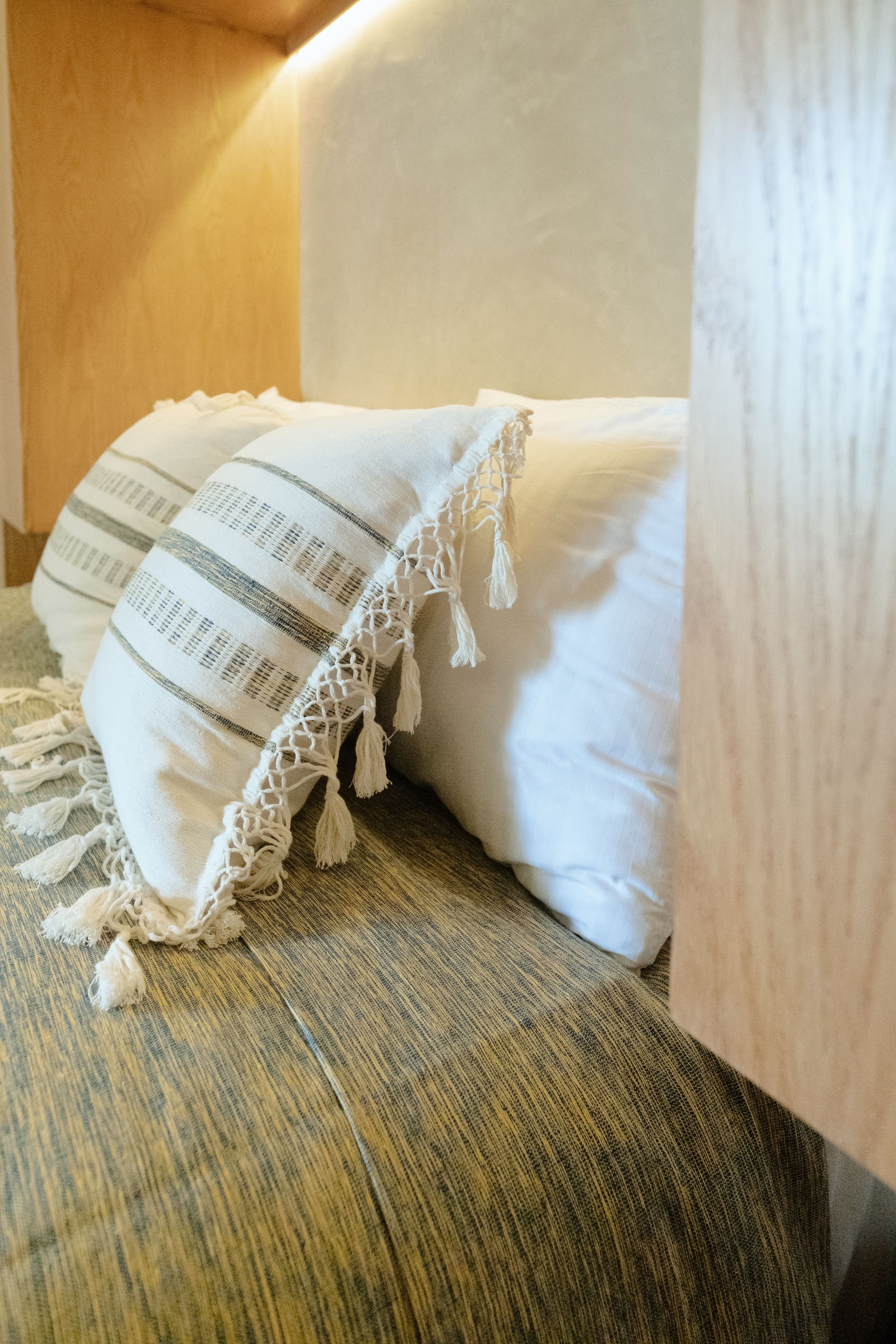 A bed with a white pillow and a striped blanket with tassels.